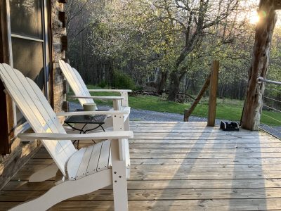 A wood-plank front porch lined with rocking chairs looking out onto a green lawn surrounded by trees.