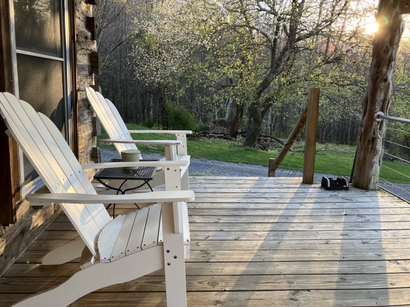 A wood-plank front porch lined with rocking chairs looking out onto a green lawn surrounded by trees.